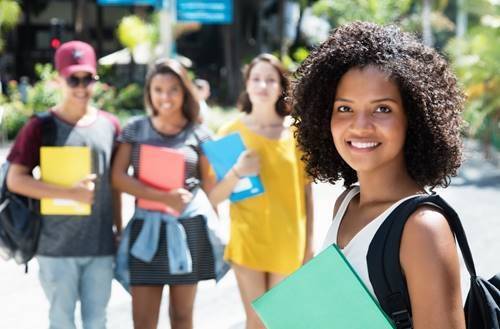 Young woman holding a binder with a backpack and other students behind her. 