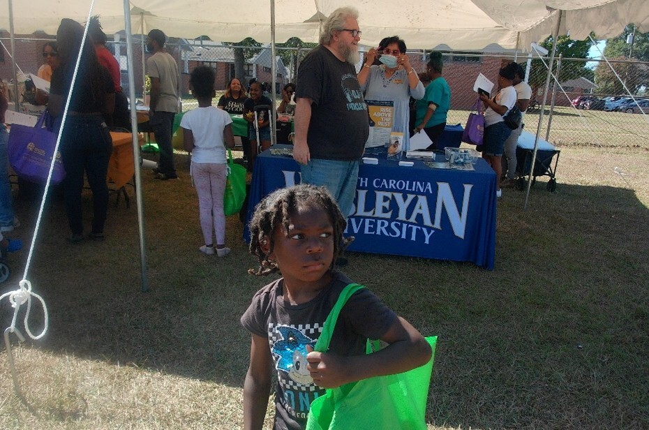 A young boy holding a greenbag in front of the North Carolina Wesleyan University table.