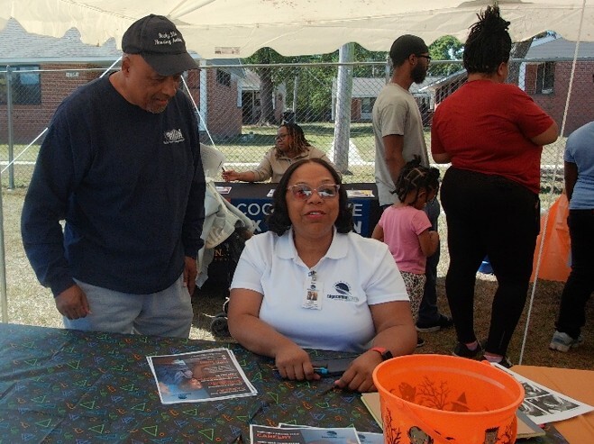 A man talking to a woman at table under a tent.