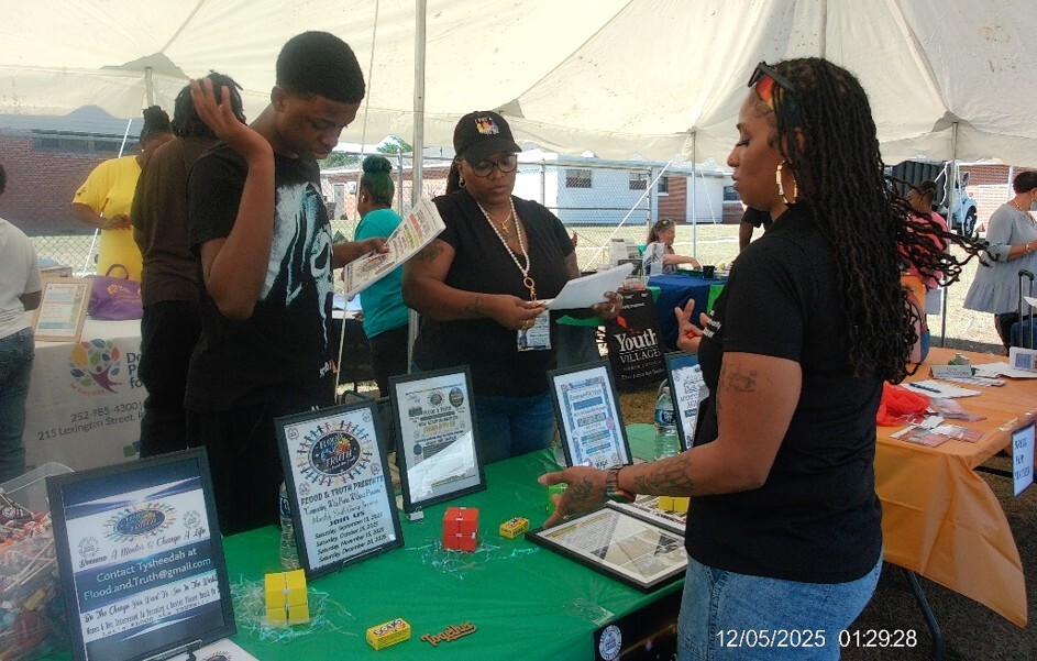 A woman talking to another woman and man at the Flood and Truth table.