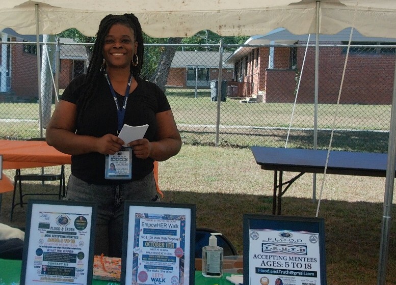 A woman stands and smiles for a picture at the flood and truth table.