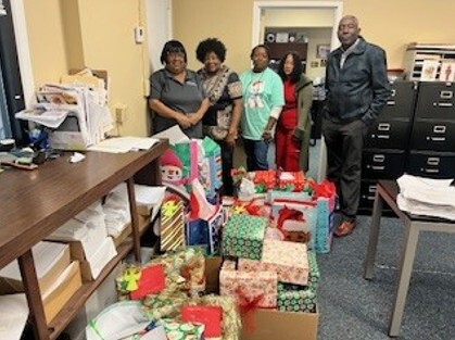 Five people stand and smile for a picture, with a table full of gifts.