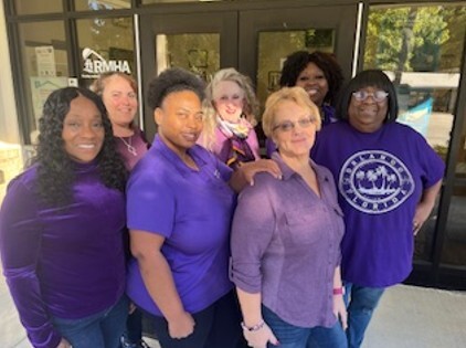 Seven women wearing purple stand and smile for a picture.